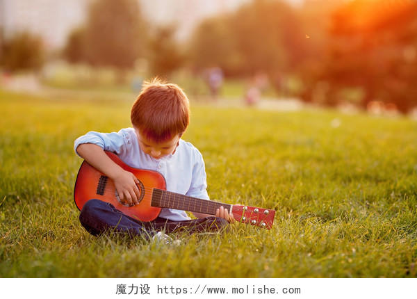 可爱的男孩坐在日落的草地上
